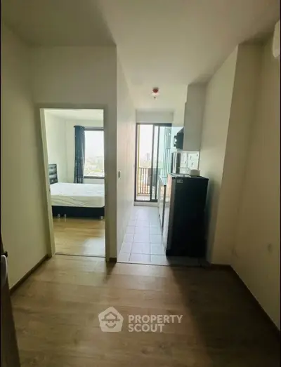 Modern apartment interior with bedroom and balcony view, featuring sleek wooden flooring and compact kitchen area.