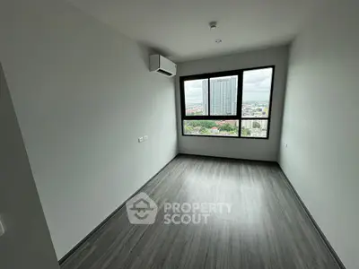 Spacious bedroom with large window offering city view and modern flooring.