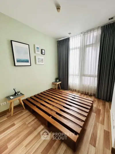 Minimalist bedroom with wooden floor and bed frame, large window with curtains, and wall art.