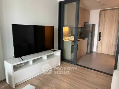 Modern apartment interior with sleek kitchen and spacious living area featuring a large TV.