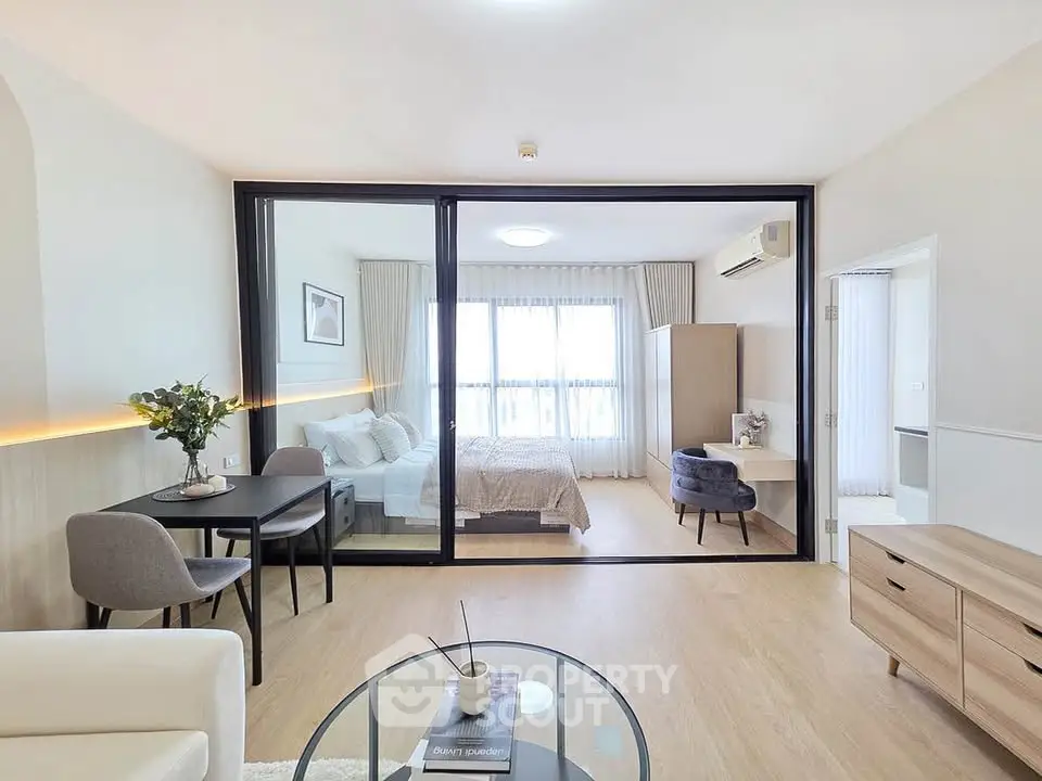 Modern open-plan living room with glass partition leading to a stylish bedroom, featuring elegant decor and natural light.