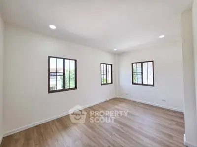 Spacious empty room with wooden flooring and large windows offering natural light.