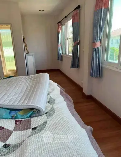 Cozy bedroom with large windows and elegant curtains, featuring a comfortable bed and wooden flooring.