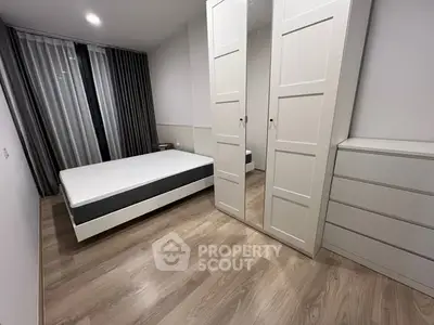 Modern minimalist bedroom with sleek white furniture and hardwood floors.