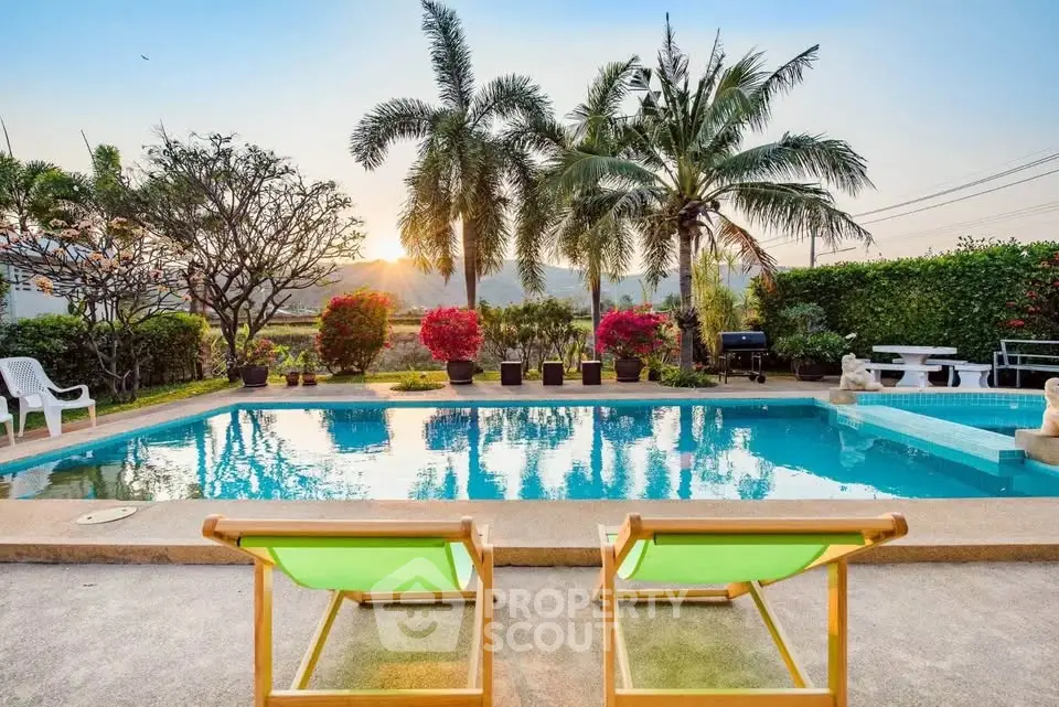 Luxurious tropical poolside with palm trees and mountain view at sunset.