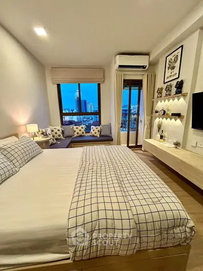 Modern bedroom with city view, stylish decor, and cozy seating area by the window.