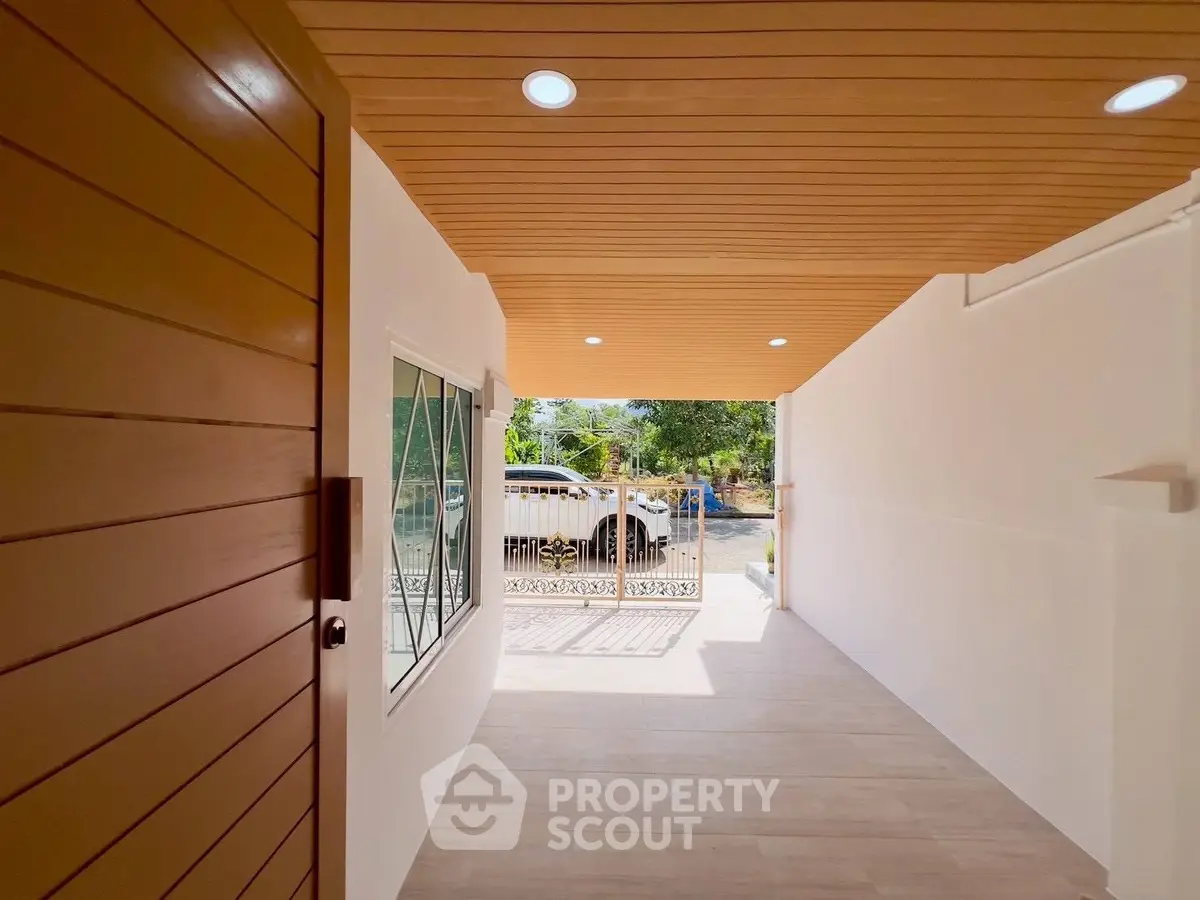 Modern entrance with wooden ceiling and large window, leading to a bright outdoor area.