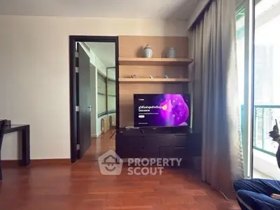 Modern living room with wooden flooring and balcony view, featuring a sleek TV setup and elegant decor.