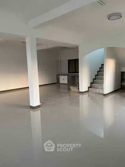 Spacious open-plan living area with glossy tiled floors and modern staircase, ideal for customization.