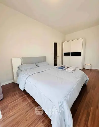 Spacious bedroom with modern decor and wooden flooring, featuring a comfortable bed and ample storage space.
