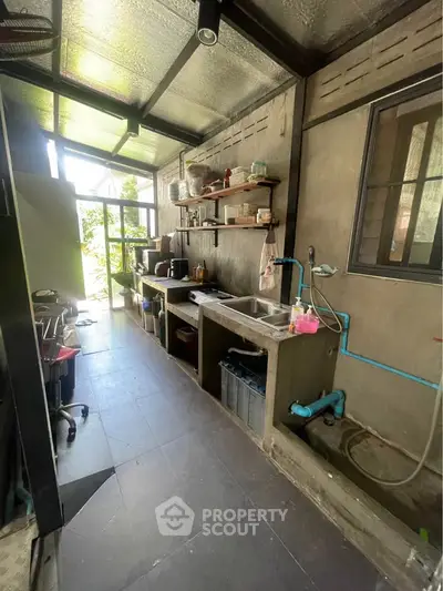 Industrial-style kitchen with concrete countertops and open shelving, featuring natural light from large windows.