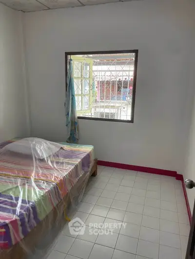 Cozy bedroom with colorful bedding and window view, ideal for a small apartment.