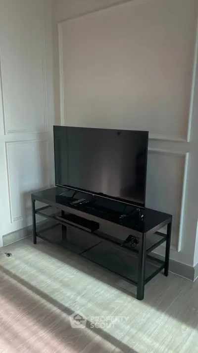 Modern living room with sleek black TV stand and flat-screen TV, elegant wall paneling, and wooden flooring.
