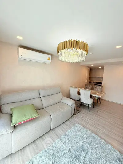 Elegant living room with plush sofa, modern chandelier, and dining area in open layout apartment.