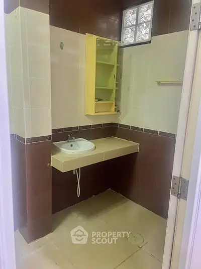 Compact bathroom with beige and brown tiles, featuring a small sink and mirror cabinet.