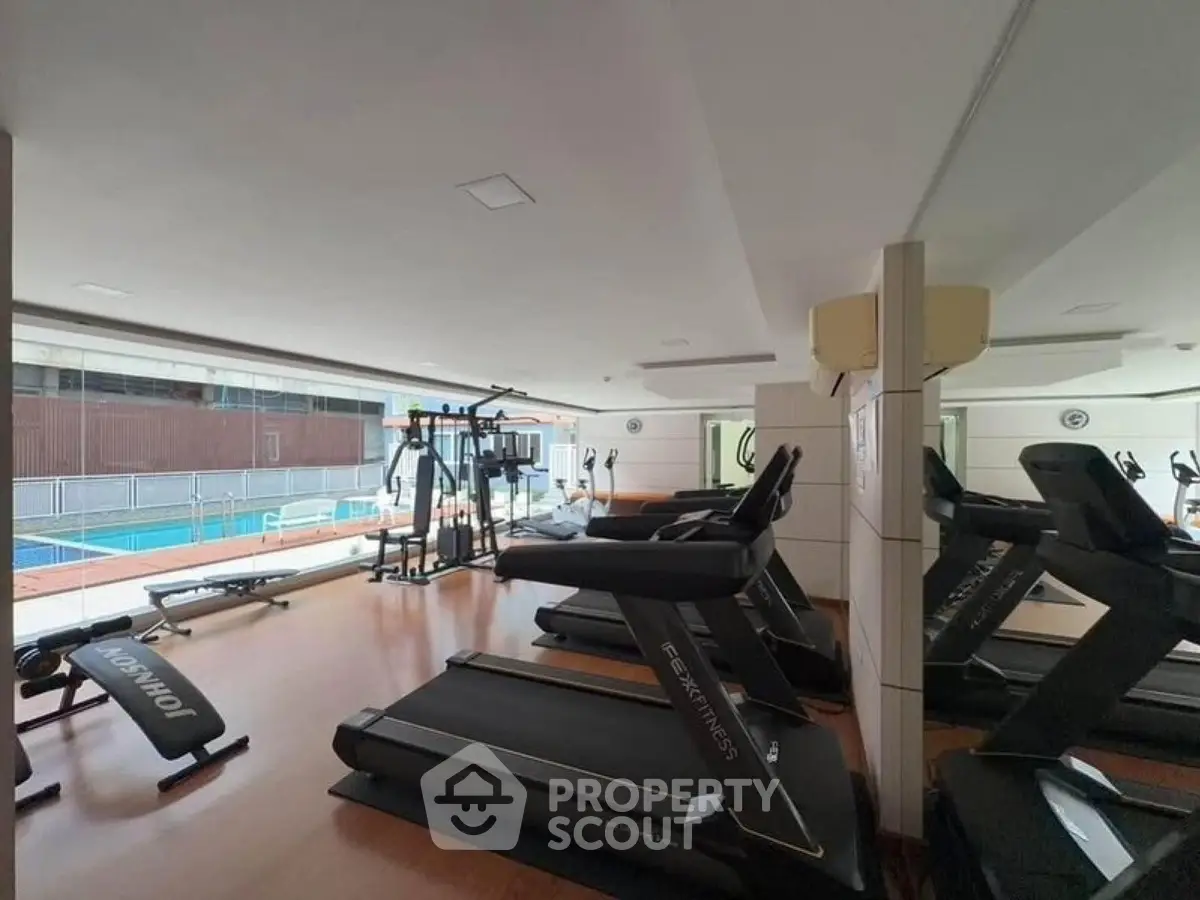 Modern gym with treadmills and pool view in luxury apartment complex.