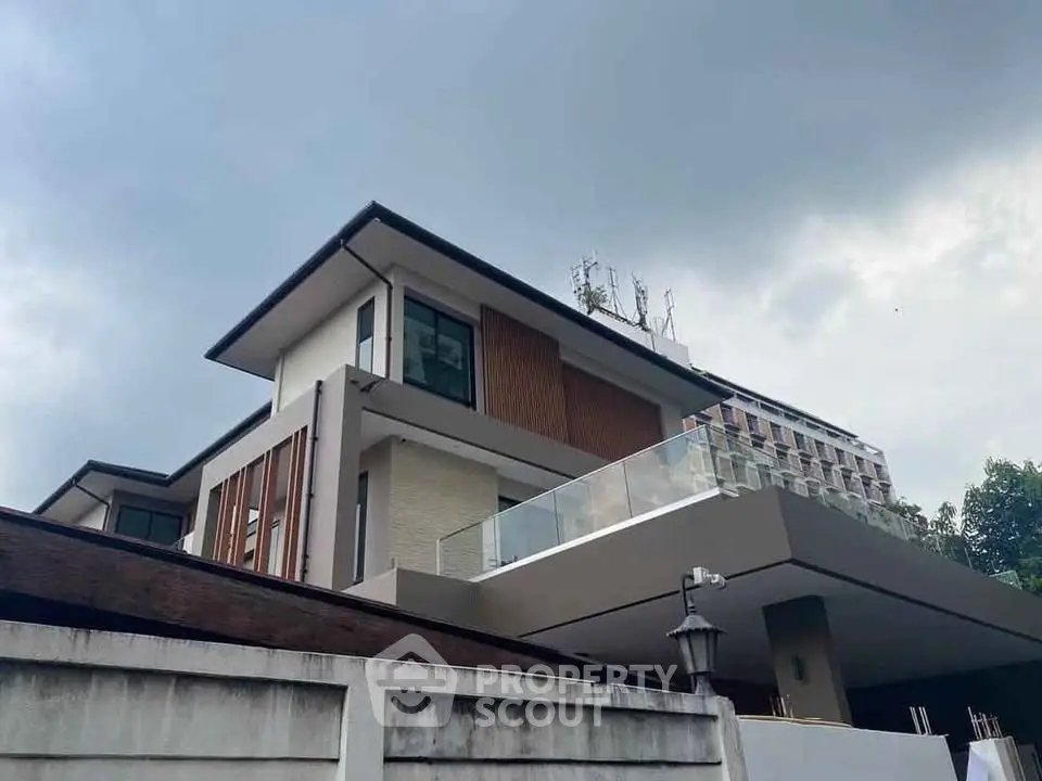 Modern multi-story house with sleek design and spacious balcony under a cloudy sky.