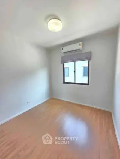 Bright empty room with wooden flooring and air conditioning, perfect for customization.