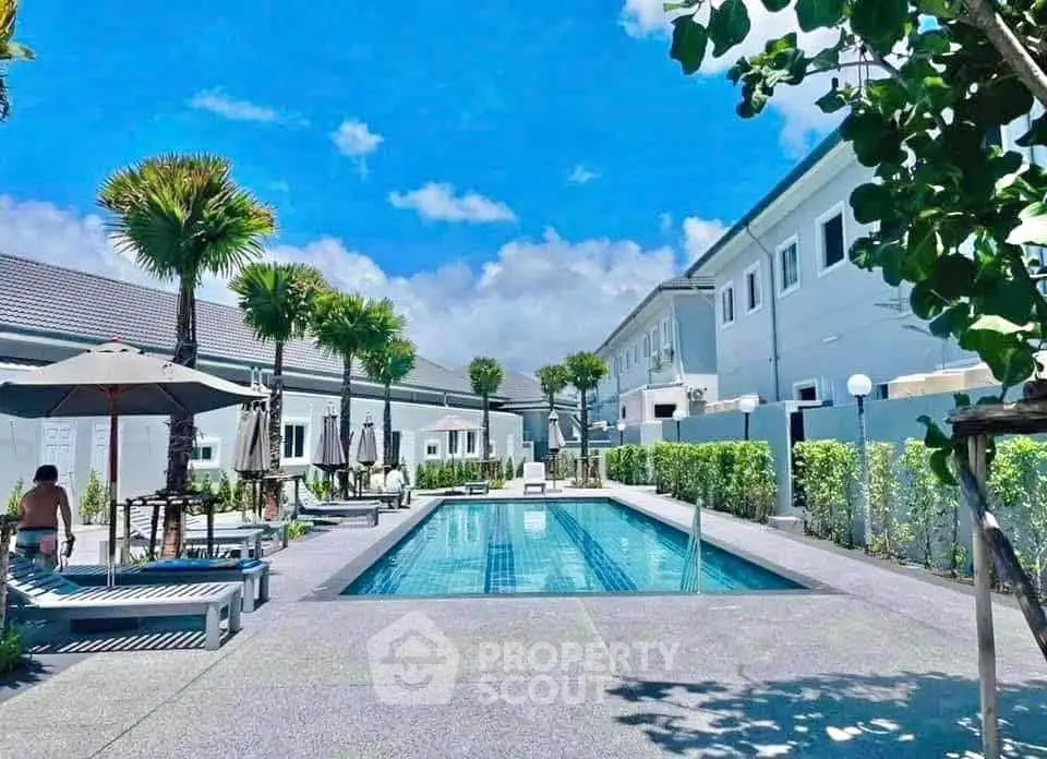Luxurious residential complex with a pristine swimming pool and lush greenery under a clear blue sky.