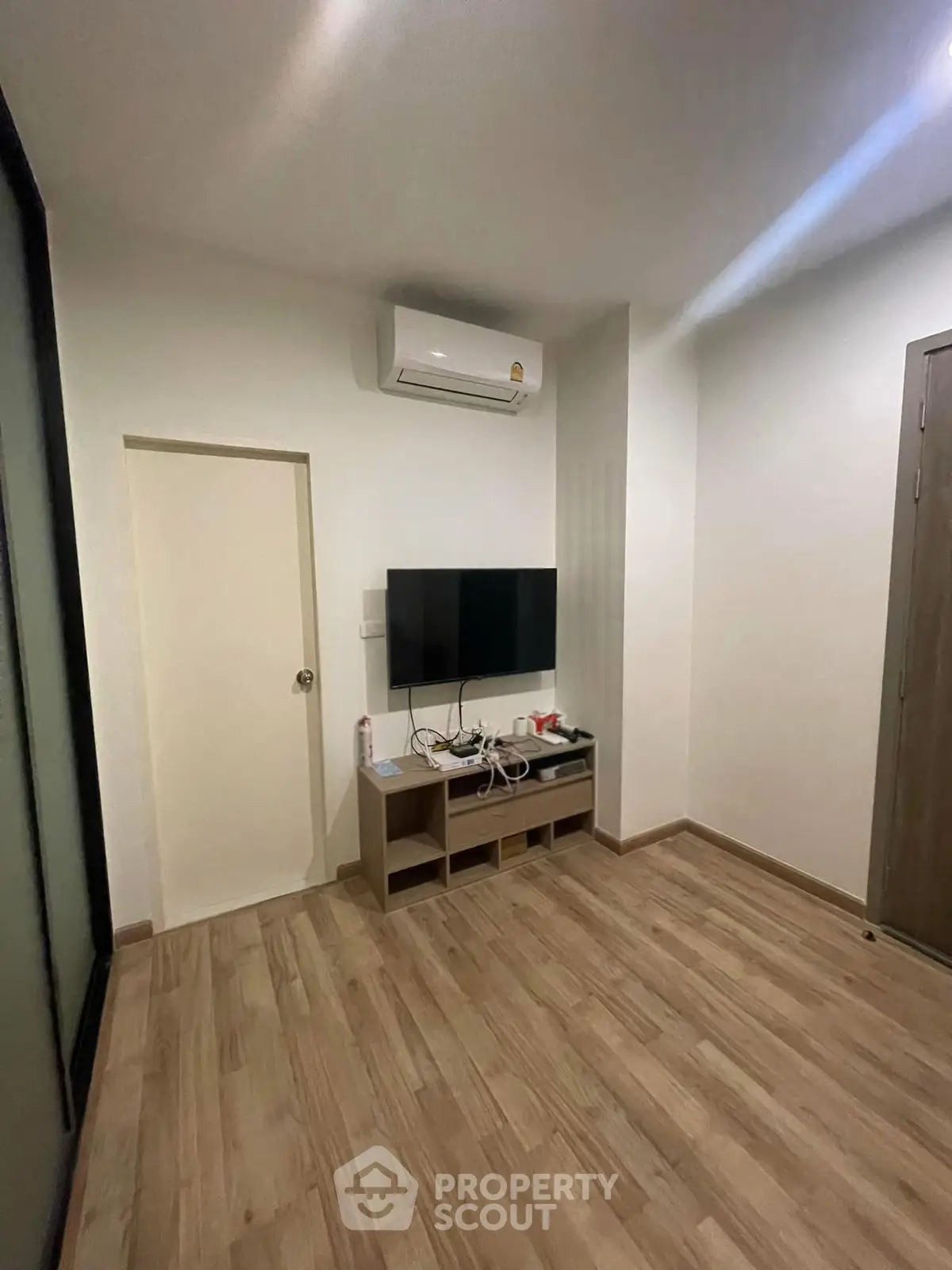 Modern minimalist living room with wooden flooring and wall-mounted TV.