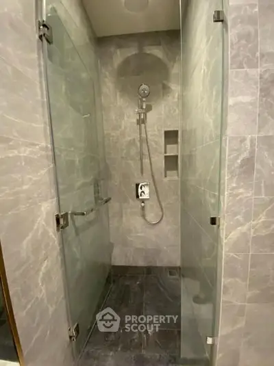 Modern glass-enclosed shower with sleek gray tiles and built-in shelving.