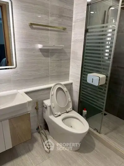 Modern bathroom with sleek design featuring toilet, sink, and glass shower enclosure.