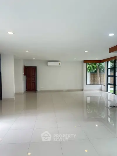 Spacious modern living room with large windows and glossy tiled floors, perfect for natural light and open living.