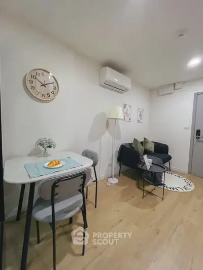 Cozy living room with modern decor and dining area, featuring wall clock and air conditioning.