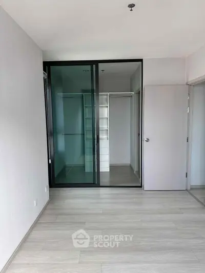 Spacious modern bedroom with sleek glass wardrobe and light wood flooring