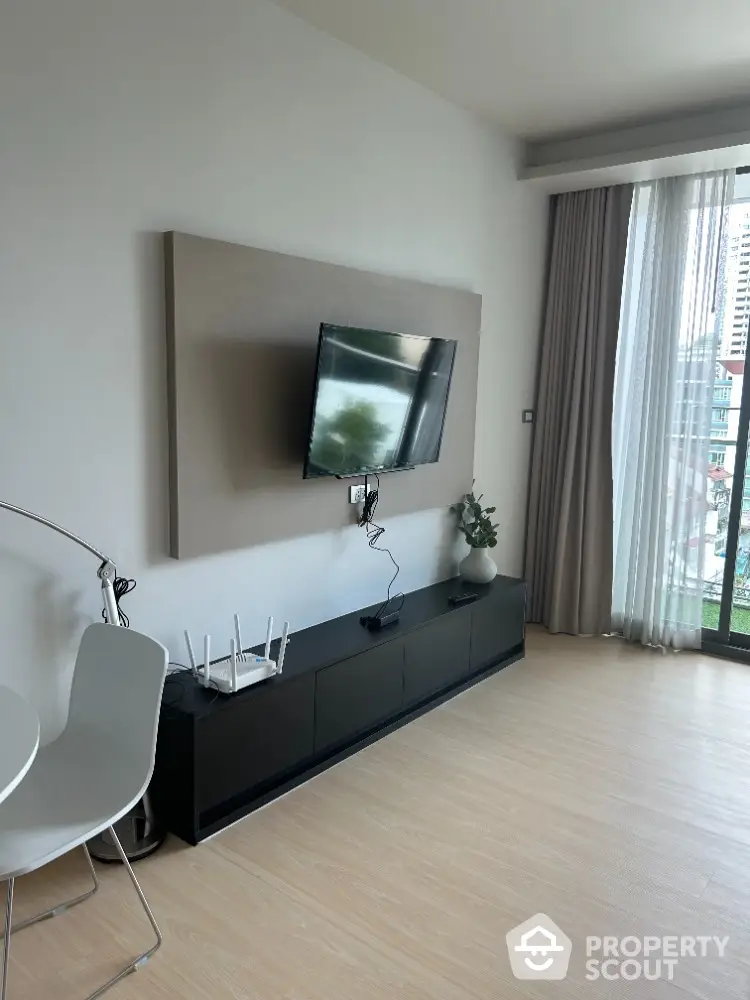 Modern living room with mounted TV and sleek furniture, featuring large window with city view.