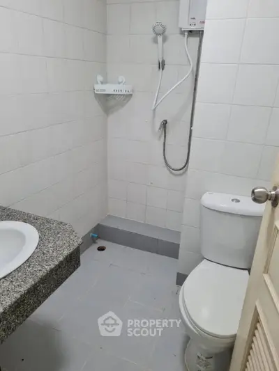 Compact bathroom with shower, toilet, and granite countertop sink in modern apartment.