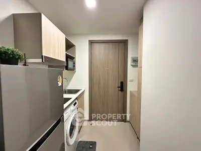 Modern compact kitchen with washing machine and stainless steel fridge in sleek apartment.