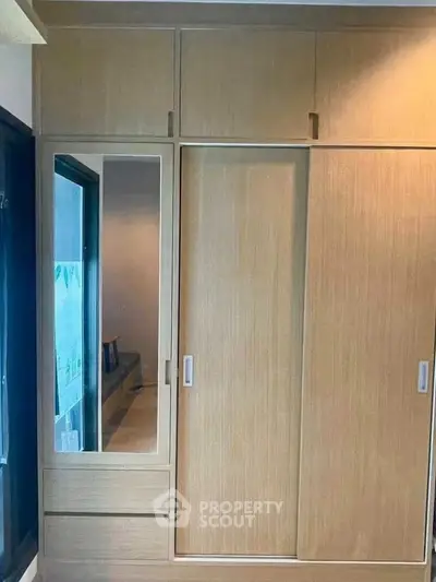 Spacious wooden wardrobe with sliding doors and mirror in modern bedroom.