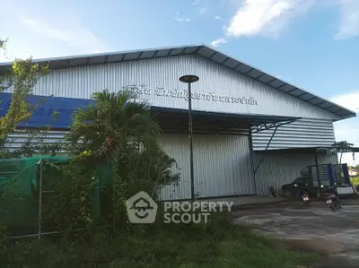 Industrial warehouse exterior with metal siding and blue roof, surrounded by greenery and clear sky.