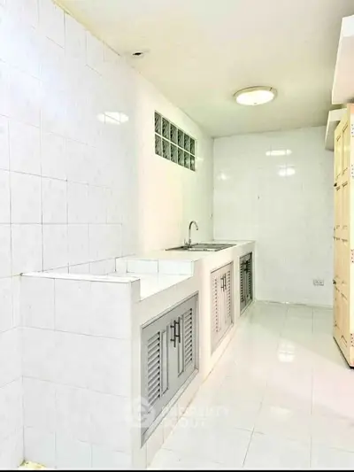 Spacious white-tiled kitchen with ample storage and sleek design.