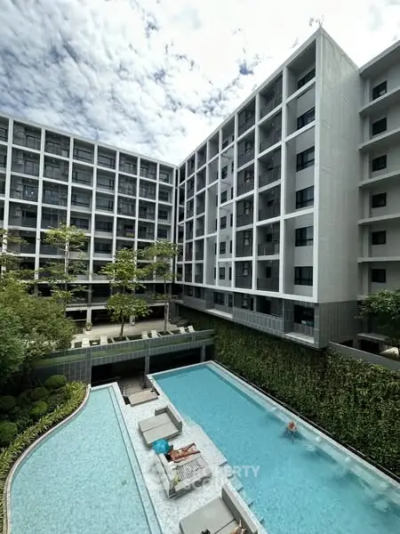 Modern apartment complex with pool and lush greenery under a blue sky.