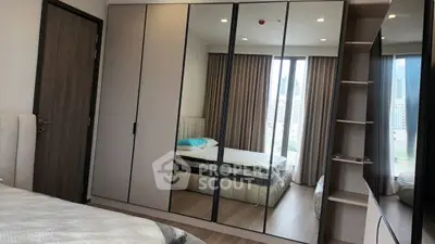 Modern bedroom with mirrored wardrobe and city view, featuring elegant decor and ample natural light.