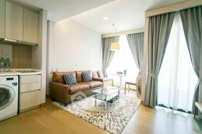 Modern living room with cozy sofa, washing machine, and elegant curtains in a bright apartment.