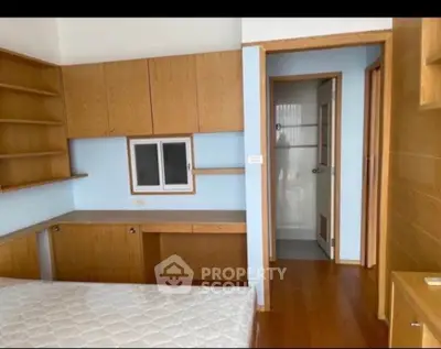 Spacious bedroom with built-in wooden shelves and desk, adjacent to a modern bathroom.