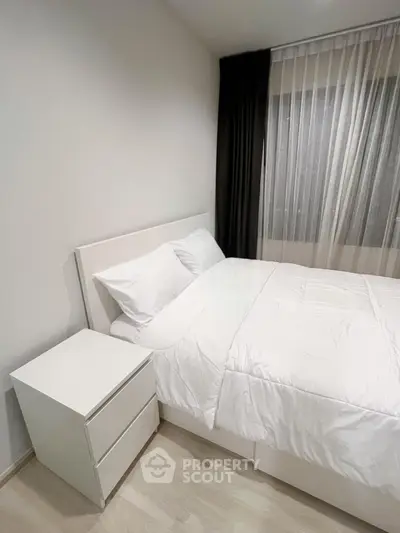 Modern minimalist bedroom with white bed and nightstand, featuring sheer curtains and natural light.