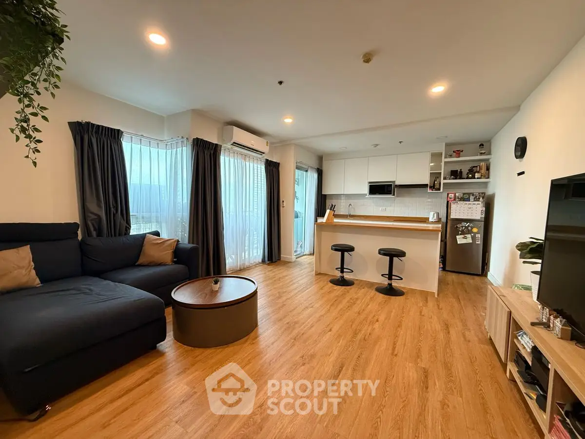 Modern open-plan living room with kitchen, featuring sleek furniture and wooden flooring.