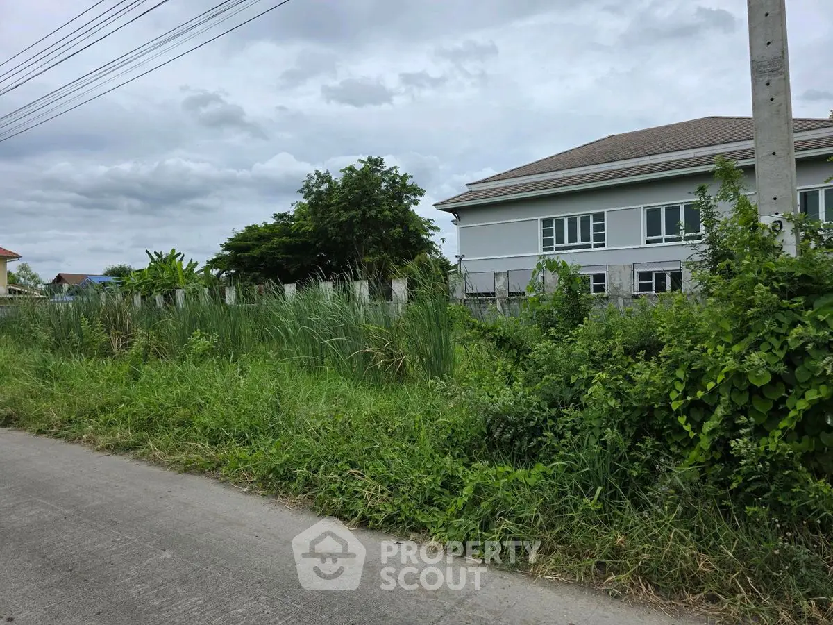 Spacious land plot with lush greenery and adjacent modern building, ideal for development.