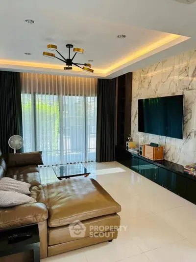 Luxurious living room with modern decor and large TV, featuring elegant lighting and marble accent wall.