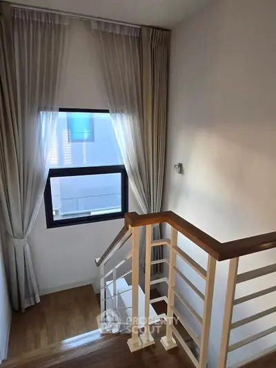Elegant staircase with wooden railing and sheer curtains in a modern home interior.