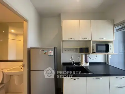 Modern kitchen with sleek cabinets, stainless steel fridge, and microwave, adjacent to a bathroom.