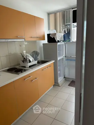 Compact kitchen with orange cabinets and modern appliances in a cozy apartment.