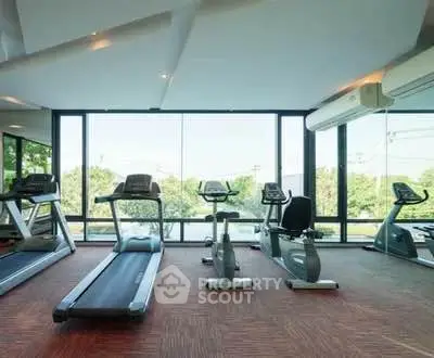 Modern gym with large windows and exercise equipment in a bright, spacious setting.
