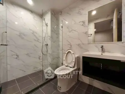 Modern bathroom with marble walls, glass shower, and sleek vanity.