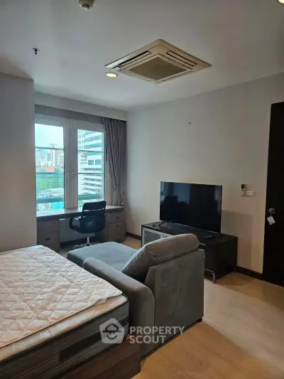 Modern studio apartment with large window and city view, featuring a cozy sofa and flat-screen TV.