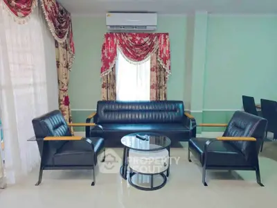 Elegant living room with black leather furniture and floral curtains, featuring a modern air conditioning unit.